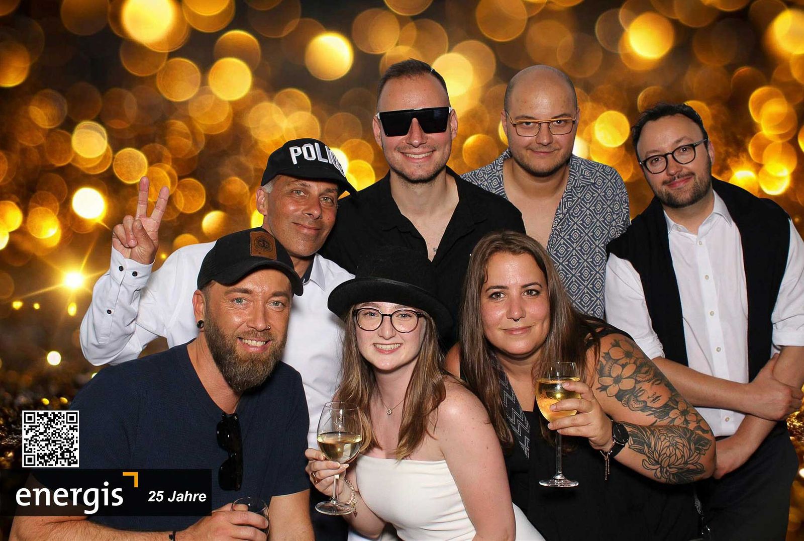 KI-Box im Klassik-Modus beim energis 25 Jahre Sommerfest Stadthalle Dillingen — sieben Gäste mit POLICE-Mütze und Champagner vor goldenem Bokeh-Backdrop, energis-Branding mit QR-Code