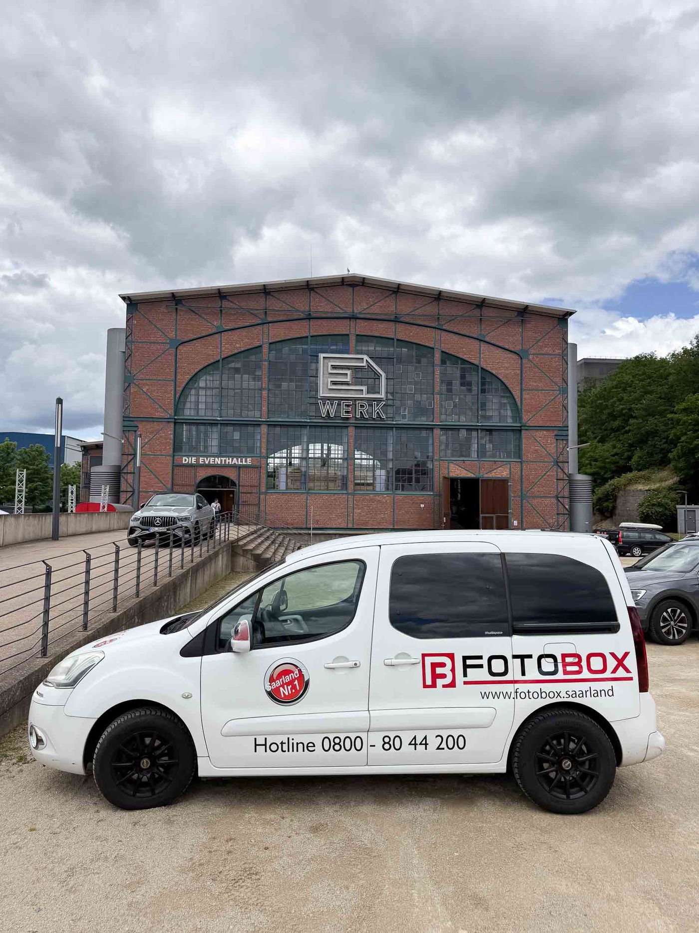 Foto-Lutz-Auslieferwagen mit FOTOBOX-Branding und Hotline 0800-80 44 200 vor dem E-Werk Saarbrücken — die Eventhalle DIE EVENTHALLE als Industrie-Backsteinkulisse