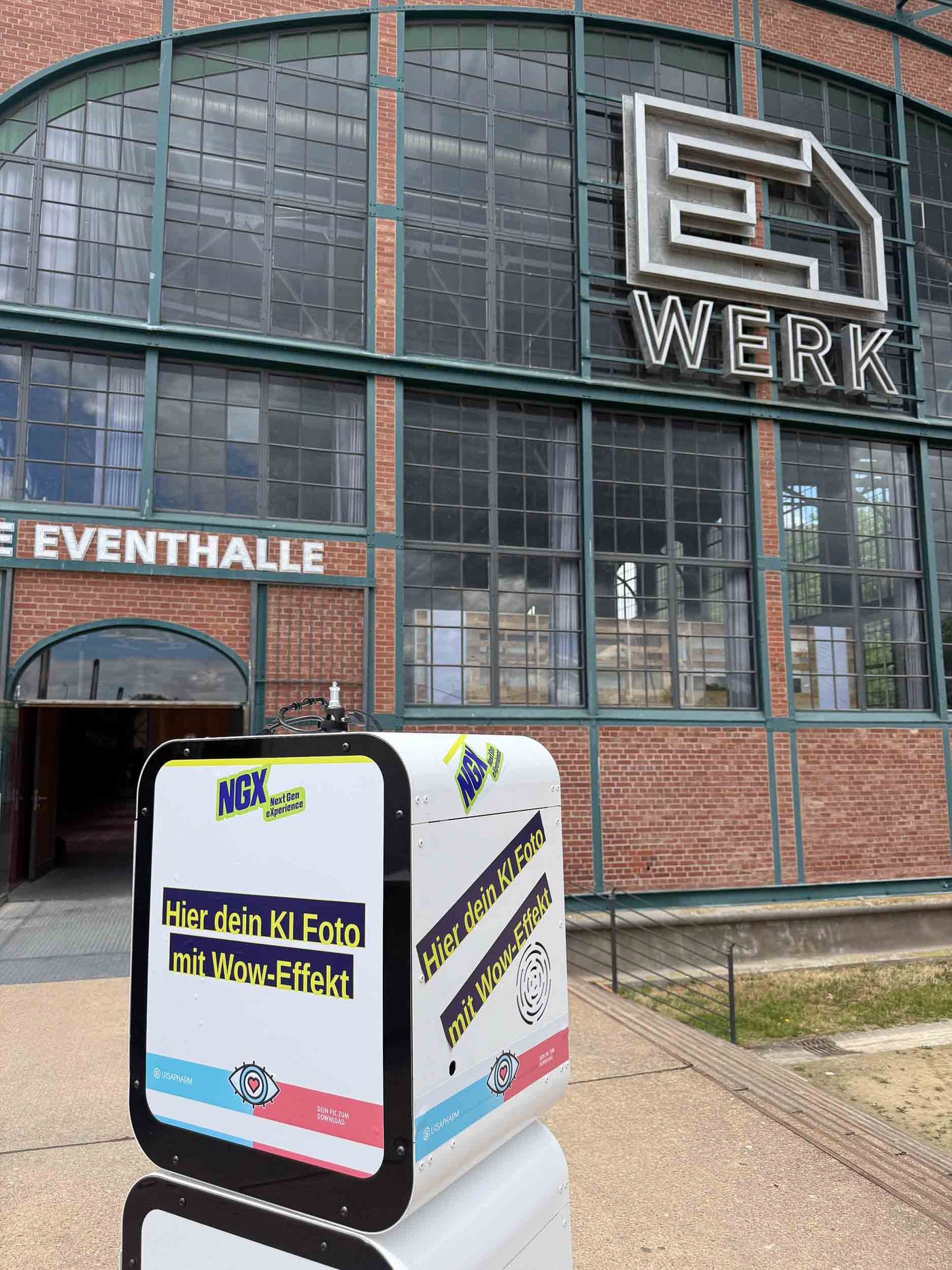 KI-Fotobox von Foto Lutz vor dem Eingang des E-Werks Saarbrücken — Hier dein KI-Foto mit Wow-Effekt Display und Ursapharm-Branding bei der NextGen eXperience, riesiges E-WERK Logo der Eventhalle im Hintergrund