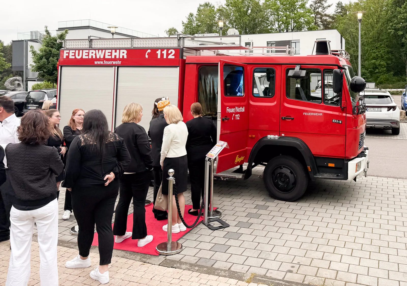 Feuerwehrbus von Foto Lutz vor Firmenevent — gut gekleidetes Publikum in der Warteschlange auf rotem Teppich, Outdoor-B2B-Setup mit Mercedes 814