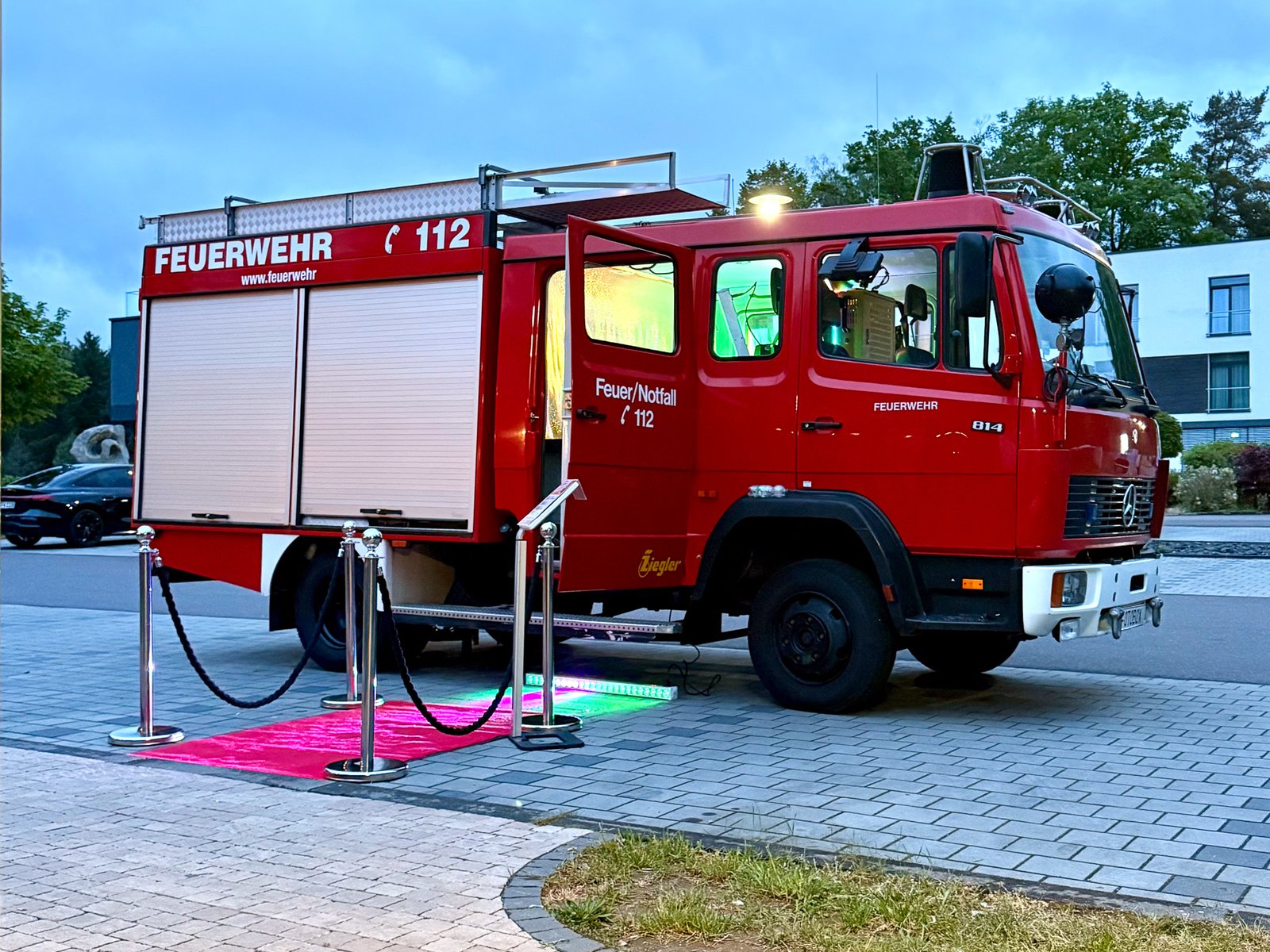 Feuerwehrbus Mercedes 814 mit ausgerolltem roten Teppich und Absperrung beim Outdoor-Event in der Dämmerung — Foto Lutz Setup
