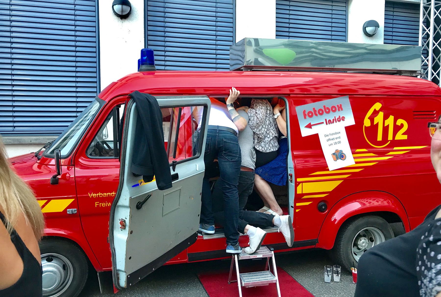 Feuerwehrbus von Foto Lutz Generation 1.0 mit fotobox-Inside-Sticker — Gäste quetschen sich gegenseitig in den Bus rein, Team-Building-Klassiker auf rotem Teppich