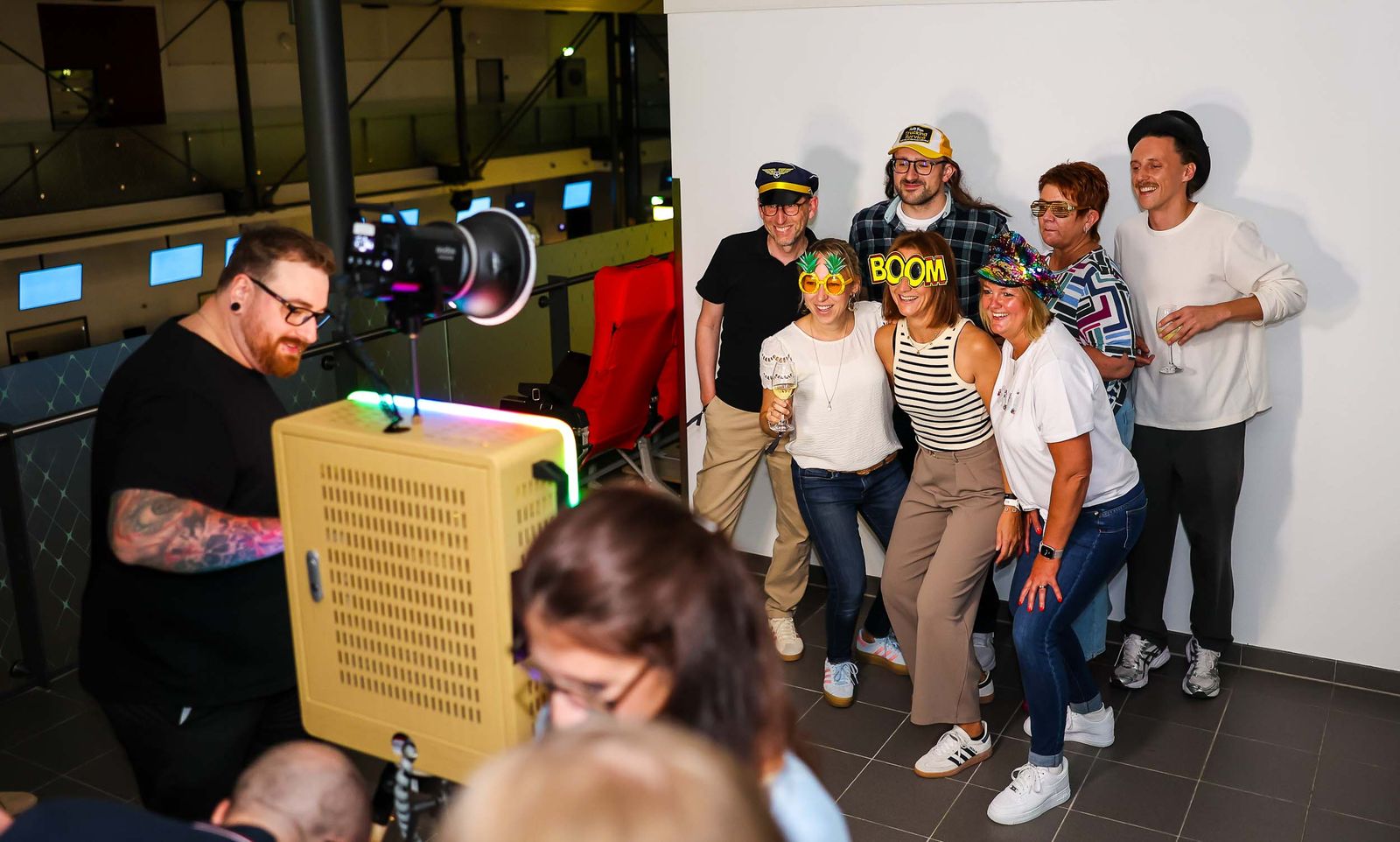 Klassik-Fotobox am Flughafen Saarbrücken — Markus Lutz hinter der Box mit Studio-Blitz, Gästegruppe mit Pilotenmütze und Spaßbrille beim Foto