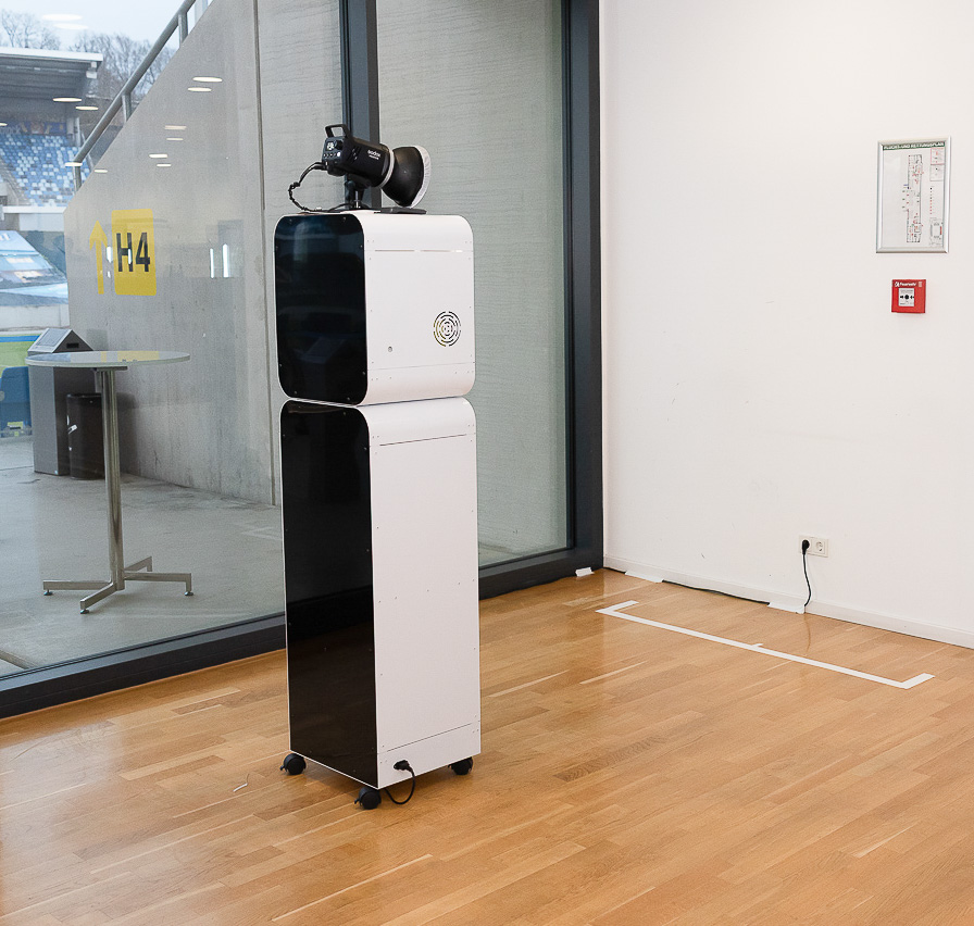 KI-Fotobox von Foto Lutz — minimalistisch designte Säule in Weiß und Schwarz auf Rollen, auf Wunsch mit Kundenbranding im individuellen CI beklebt oder beschriftet