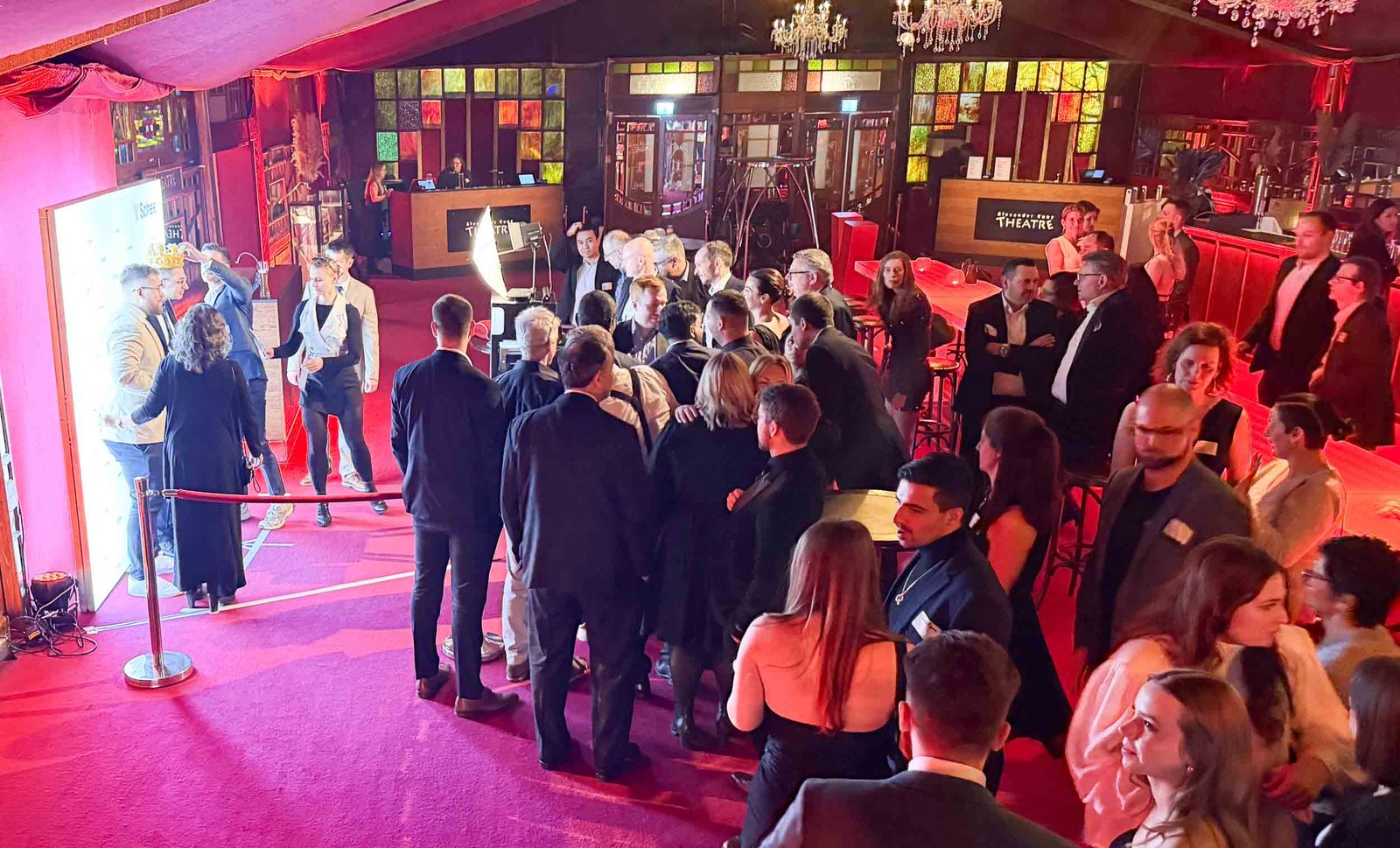 Fotobox von Foto Lutz im Kunz Theatre Saarbrücken — typische Schlange im Wartebereich am Eventabend, edel gekleidete Gäste vor dem KUNZ THEATRE Schild und Bühnenkulisse