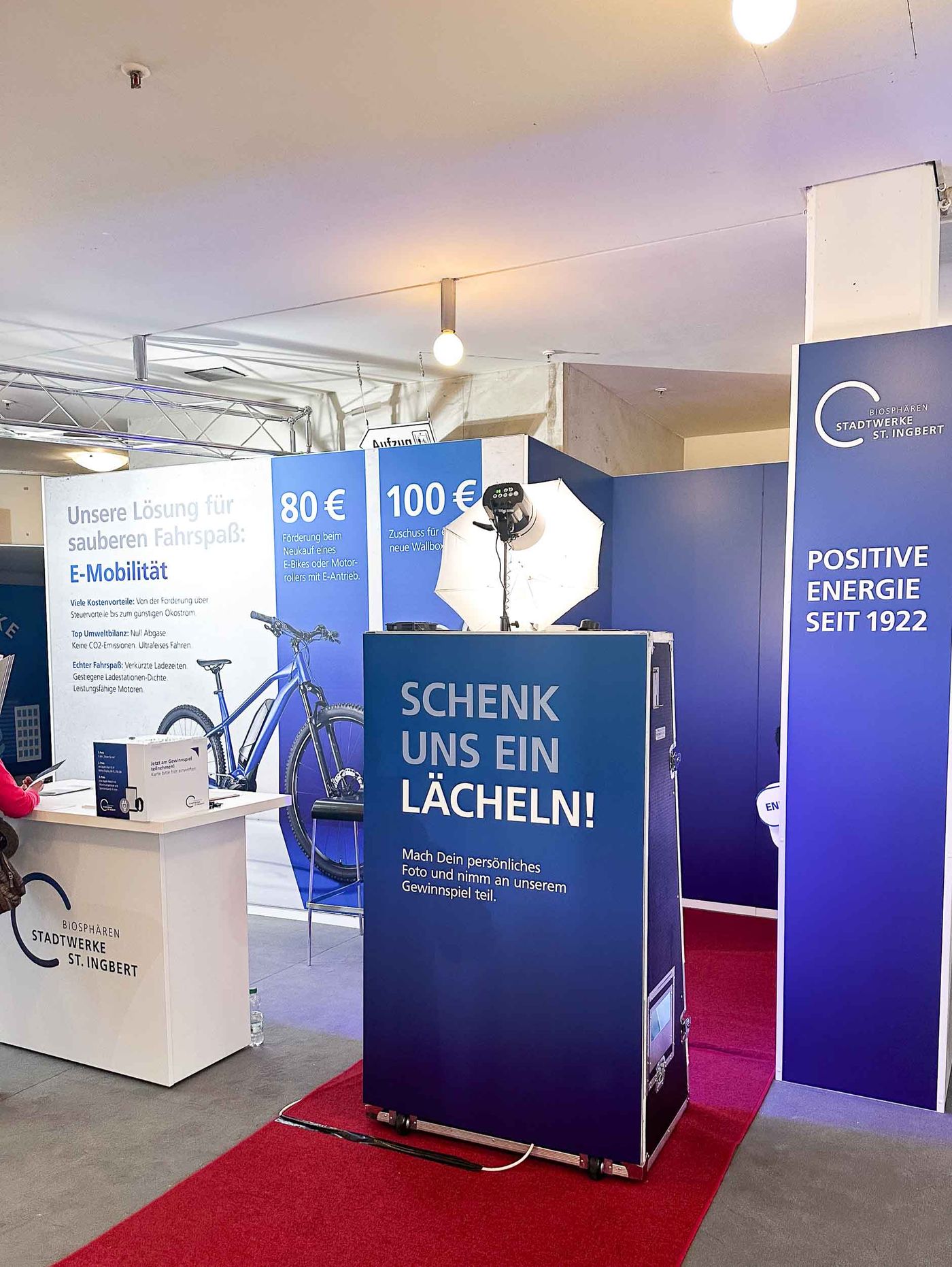 Magic Mirror Fotospiegel auf der Ingobertus-Messe St. Ingbert — vollflächig in Stadtwerke-St-Ingbert-CI gebrandet mit SCHENK UNS EIN LÄCHELN Slogan, neben E-Mobilität-Display und Positive Energie seit 1922 Säule