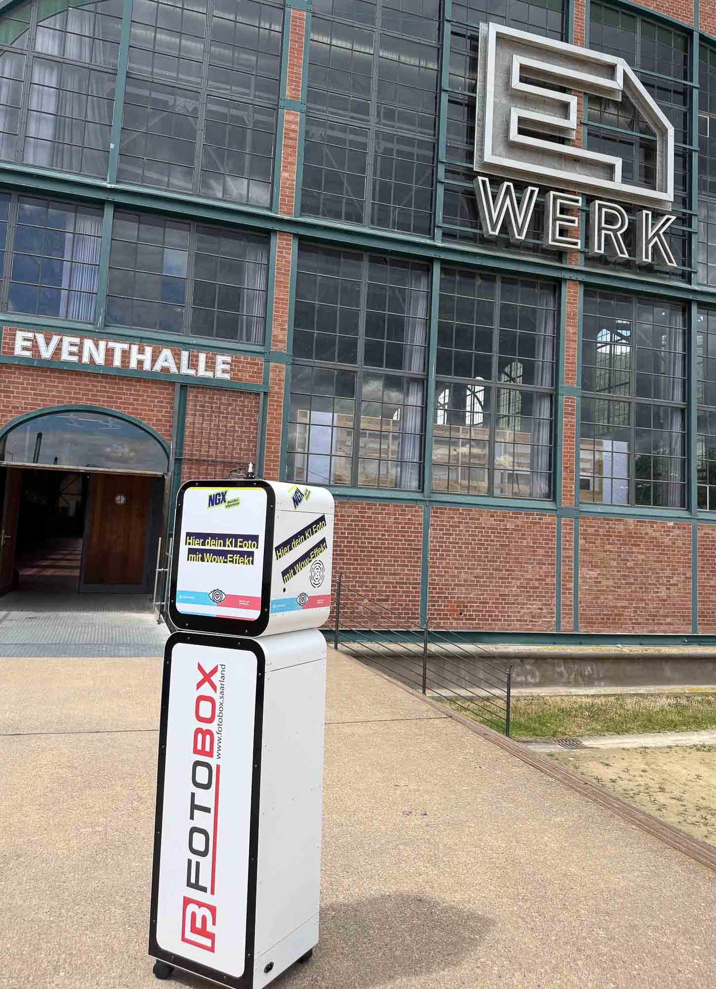 KI-Fotobox von Foto Lutz vor dem E-Werk Saarbrücken bei der Anlieferung — Box im vollen Custom-CI-Branding für NGX und Ursapharm, riesiges E-WERK Eventhalle-Logo im Hintergrund