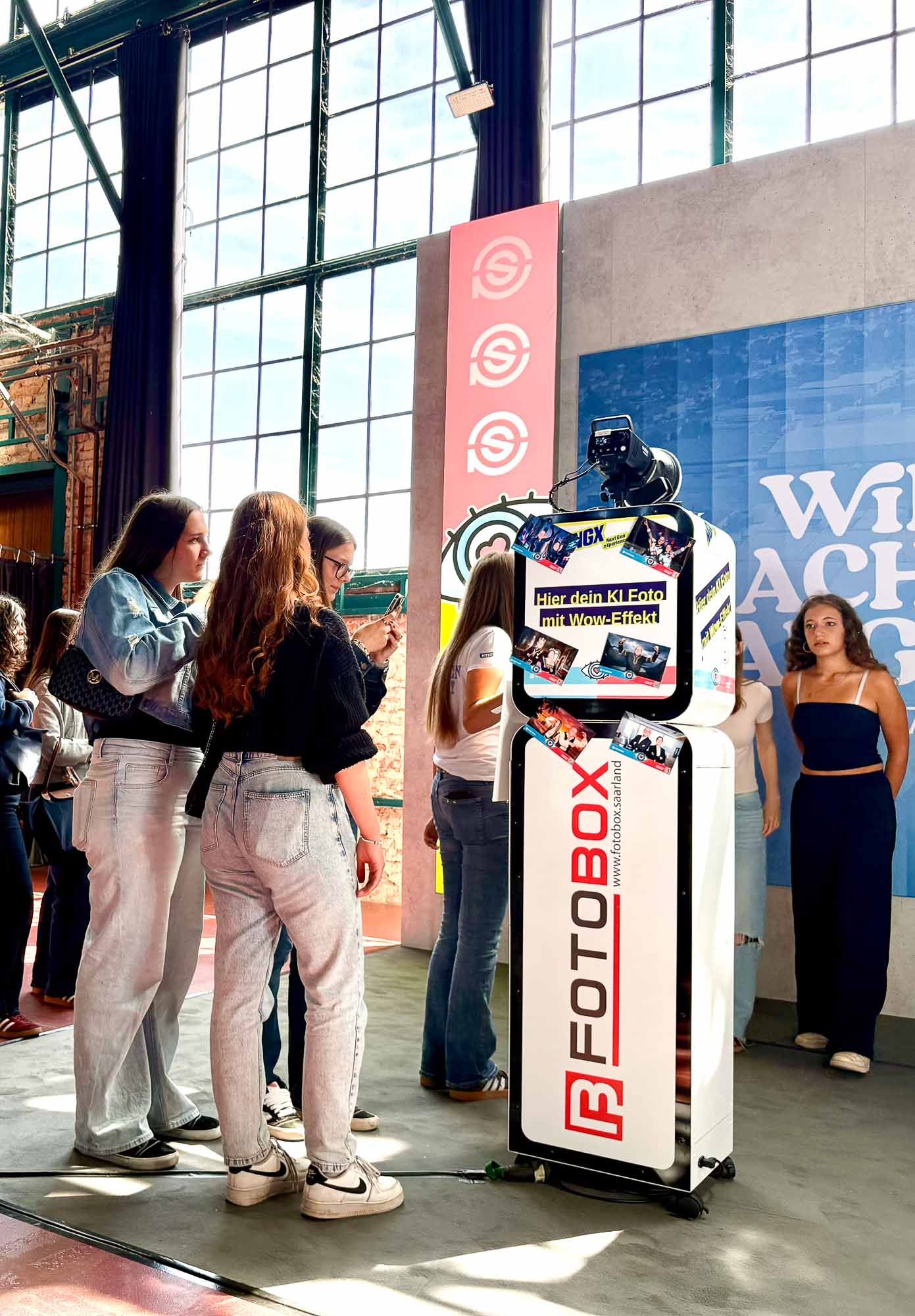Gruppe junger Frauen interagiert mit dem Touchscreen der KI-Fotobox am Ursapharm-Stand NextGen eXperience — Display zeigt Hier dein KI-Foto mit Wow-Effekt im NGX-Branding