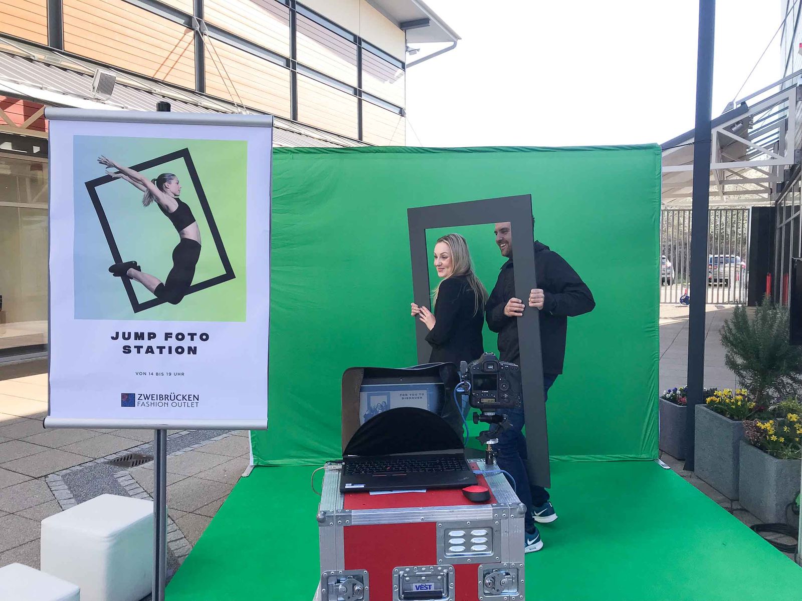Zwei Gäste posieren mit Frame-Requisite vor dem Greenscreen im Fashion Outlet Zweibrücken — JUMP FOTO STATION Roll-up und Foto-Lutz-Transportkiste