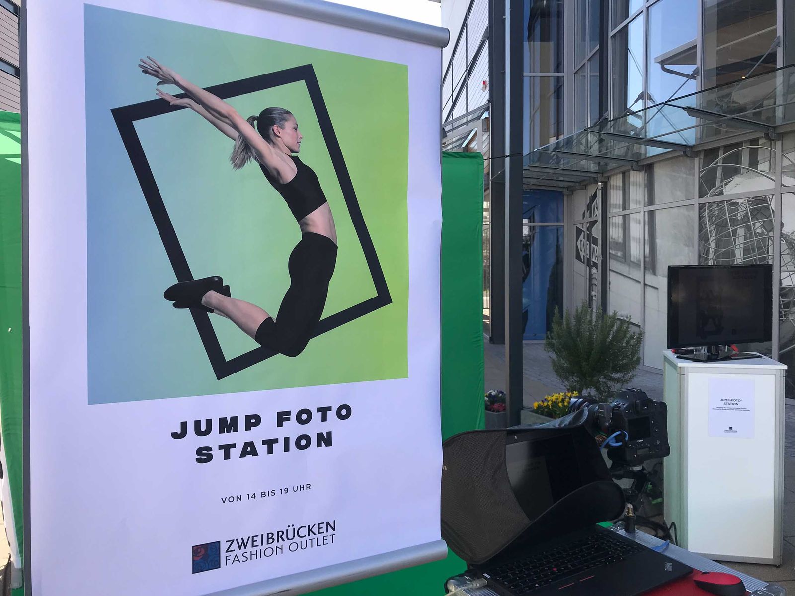 JUMP FOTO STATION Roll-up im Detail — Pose-Anleitung Sprung im Frame, Einsatzzeit VON 14 BIS 19 UHR, ZWEIBRÜCKEN FASHION OUTLET Logo, Setup mit Computer und Kamera im Fashion Outlet Zweibrücken