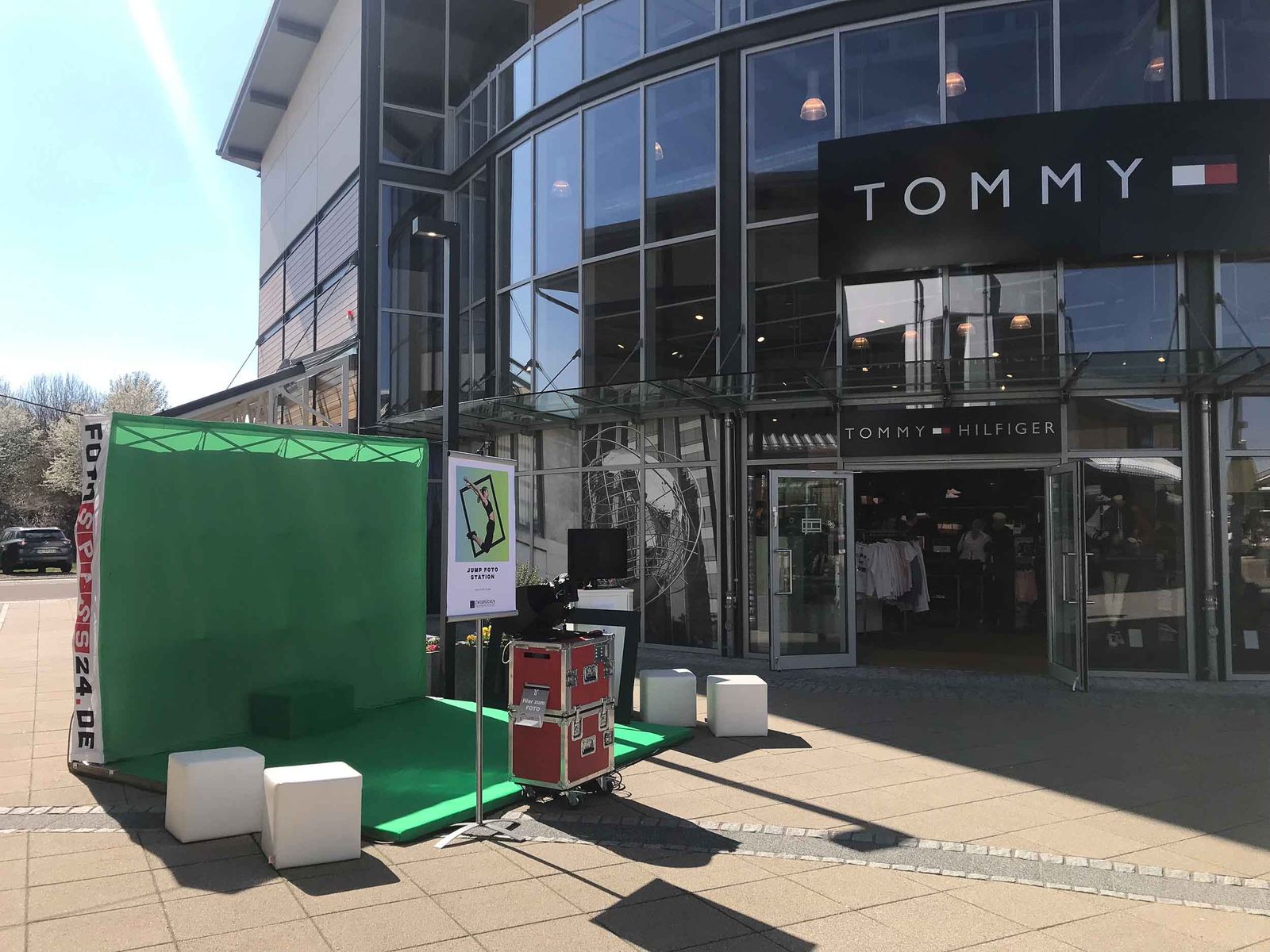 Foto Lutz mobiles Greenscreen-Studio mit Fotoprintmodul vor Tommy Hilfiger im Fashion Outlet Center Zweibrücken — grüne Backdrop-Wand, Foto-Lutz-Transportkiste, Hocker
