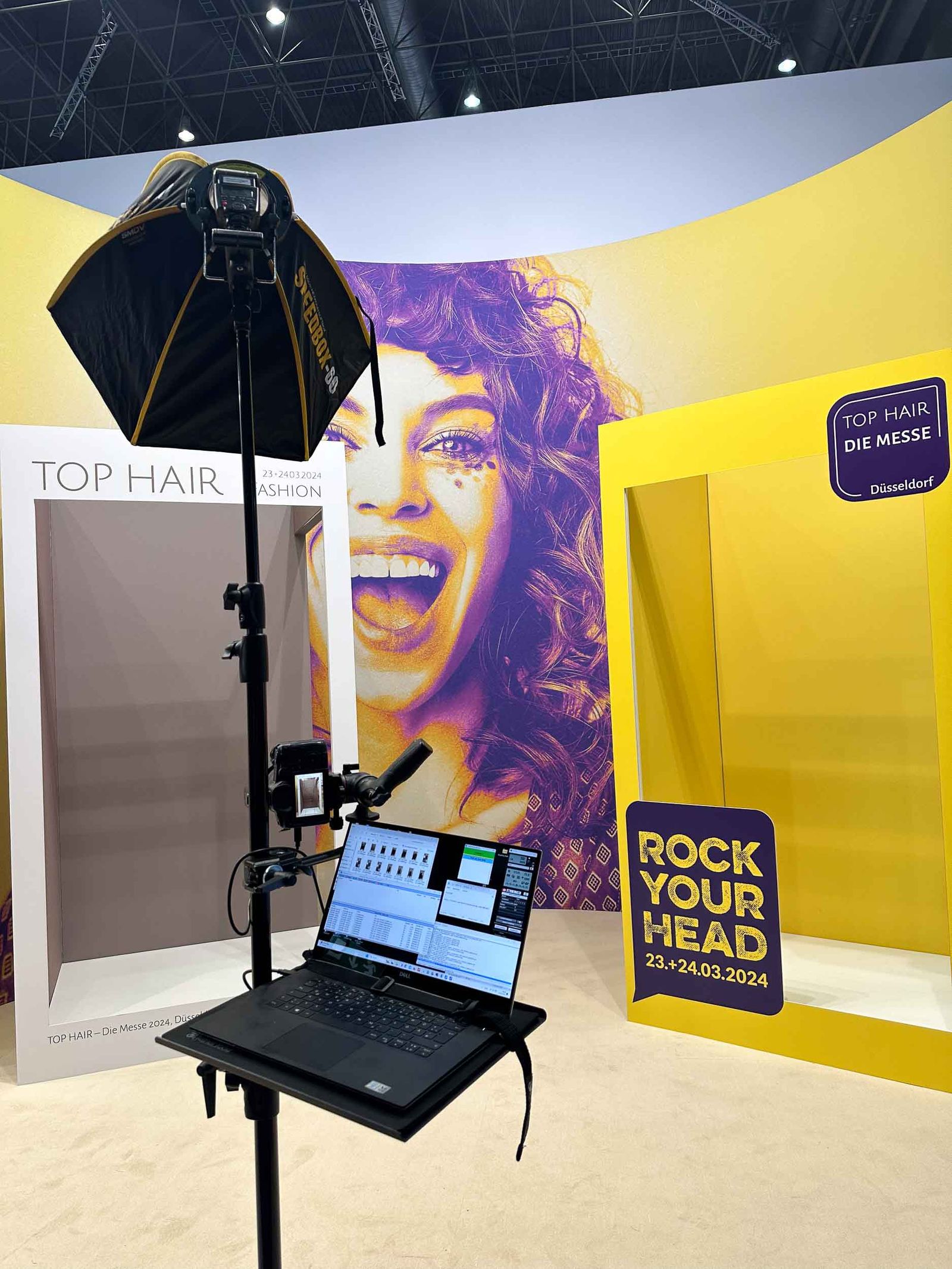 Foto Lutz Fotoprintmodul unsichtbar in den Tophair-Messebau Düsseldorf 2024 integriert — Profi-Studio-Schirm mit Laptop vor ROCK YOUR HEAD Backdrop und TOP HAIR Die Messe Branding